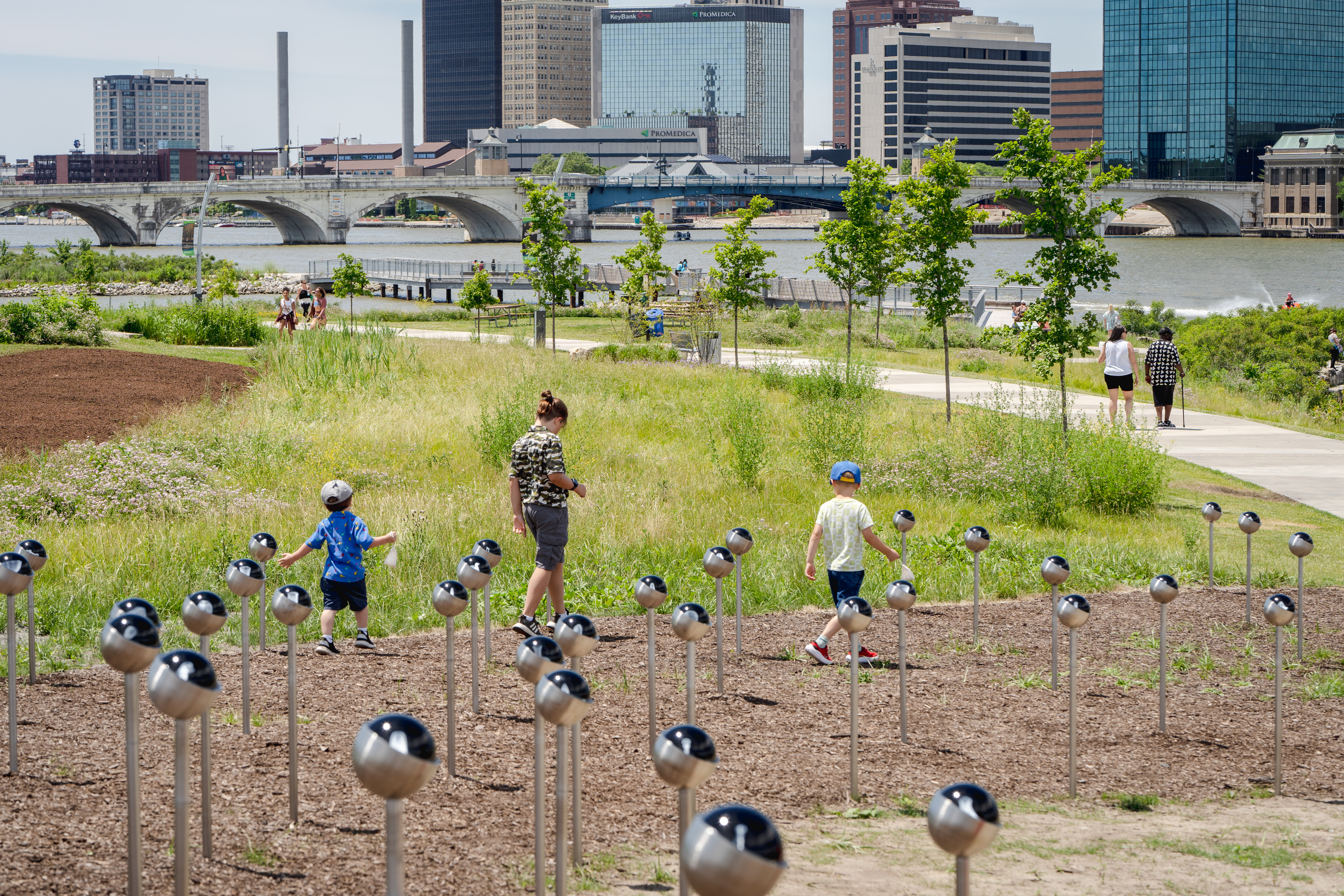 A family looks at the Field of History orbs in Glass City Metropark, with the Maumee River in the background.